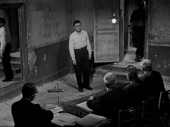 Movie still from “Orpheus” (1950), directed by Jean Cocteau – A man standing in front of a group of people in a room; Wide shot, High angle