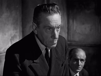 Movie still from “Orpheus” (1950), directed by Jean Cocteau – A black and white photo of a man in a suit and tie; Close Up shot, Low angle