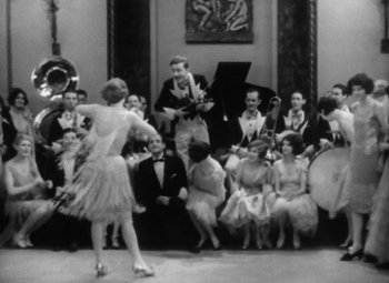 Movie still from “Our Dancing Daughters” (1928), directed by Harry Beaumont – A group of people sitting and standing in a room; Wide shot, High angle