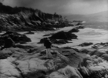 Movie still from “Our Dancing Daughters” (1928), directed by Harry Beaumont – A man standing on a rocky shore holding a fishing rod; Extreme Wide shot, High angle