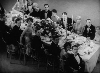 Movie still from “Our Dancing Daughters” (1928), directed by Harry Beaumont – A group of people sitting at a table with flowers on top of the table; Wide shot, High angle