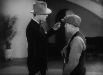 Movie still from “Our Dancing Daughters” (1928), directed by Harry Beaumont – A man in a suit and a man in a hat talking to each other; Medium shot, Over the shoulder angle