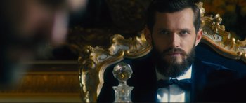 Movie still from “Our Kind of Traitor” (2016), directed by Susanna White – A man in a tuxedo sitting in front of an ornate chair; Close Up shot, Over the shoulder angle