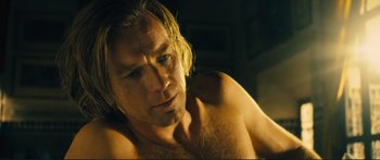 Movie still from “Our Kind of Traitor” (2016), directed by Susanna White – A man with long blonde hair and no shirt is posing for the camera; Close Up shot, Low angle