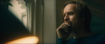 Movie still from “Our Kind of Traitor” (2016), directed by Susanna White – A man looking out of a window with his hand to his face; Close Up shot, Low angle