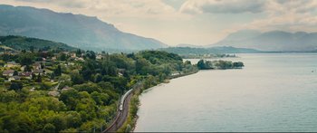 Movie still from “Our Kind of Traitor” (2016), directed by Susanna White – A train traveling on tracks next to a body of water; Extreme Wide shot, High angle
