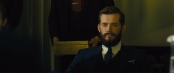 Movie still from “Our Kind of Traitor” (2016), directed by Susanna White – A man in a suit and tie with a beard; Close Up shot, Over the shoulder angle