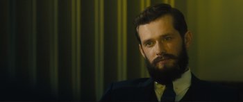 Movie still from “Our Kind of Traitor” (2016), directed by Susanna White – A man with a long beard and a suit; Close Up shot, Over the shoulder angle