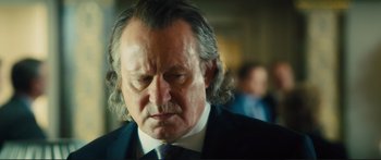Movie still from “Our Kind of Traitor” (2016), directed by Susanna White – An older man in a suit and tie looking down; Close Up shot, Over the shoulder angle