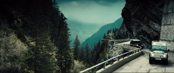 Movie still from “Our Kind of Traitor” (2016), directed by Susanna White – A view of a mountain with a road going through it; Extreme Wide shot, High angle