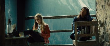 Movie still from “Our Kind of Traitor” (2016), directed by Susanna White – A woman sitting on top of a wooden railing next to a chair; Medium shot, Low angle