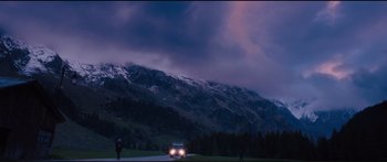 Movie still from “Our Kind of Traitor” (2016), directed by Susanna White – A car driving down a road in front of a mountain range; Extreme Wide shot, Low angle