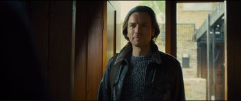 Movie still from “Our Kind of Traitor” (2016), directed by Susanna White – A man wearing a leather jacket standing next to a door; Medium shot, Over the shoulder angle