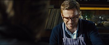 Movie still from “Our Kind of Traitor” (2016), directed by Susanna White – A man wearing glasses and an apron is smiling for the camera; Close Up shot, Over the shoulder angle