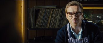 Movie still from “Our Kind of Traitor” (2016), directed by Susanna White – A man with glasses sitting in front of a wall of records; Close Up shot, Low angle