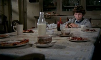Movie still from “Our Mother's House” (1967), directed by Jack Clayton – A boy sitting at a dinner table eating a hamburger; Medium shot, High angle