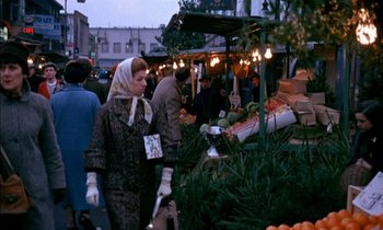 Movie still from “Our Mother's House” (1967), directed by Jack Clayton – A woman wearing a headscarf is standing in front of an outdoor market; Medium shot, High angle
