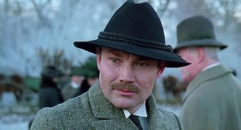 Movie still from “Out of Africa” (1985), directed by Sydney Pollack – A person wearing a suit and a hat; Close Up shot, Low angle