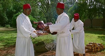 Movie still from “Out of Africa” (1985), directed by Sydney Pollack – A group of men standing next to each other holding food; Medium shot, Low angle