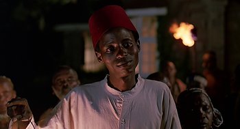 Movie still from “Out of Africa” (1985), directed by Sydney Pollack – A man wearing a red hat standing in front of a group of people; Close Up shot, Low angle