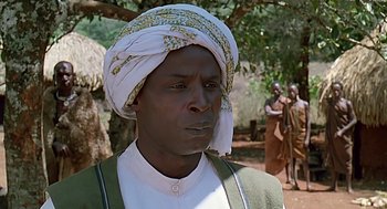 Movie still from “Out of Africa” (1985), directed by Sydney Pollack – A man with a turban is standing in front of a group of people; Close Up shot, Low angle