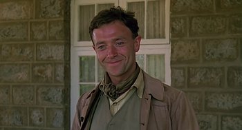 Movie still from “Out of Africa” (1985), directed by Sydney Pollack – A man in a brown jacket smiling for the camera; Close Up shot, Low angle