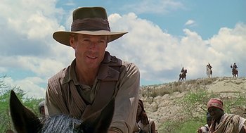 Movie still from “Out of Africa” (1985), directed by Sydney Pollack – A man in a hat and a backpack on top of a hill; Close Up shot, Low angle