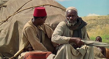 Movie still from “Out of Africa” (1985), directed by Sydney Pollack – Two men sitting next to each other on the ground; Medium shot, High angle
