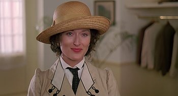 Movie still from “Out of Africa” (1985), directed by Sydney Pollack – A woman wearing a straw hat and a trench coat; Close Up shot, Over the shoulder angle
