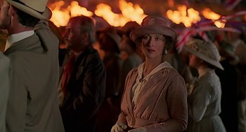 Movie still from “Out of Africa” (1985), directed by Sydney Pollack – A woman wearing a pink hat standing in front of a crowd of people; Medium shot, Over the shoulder angle