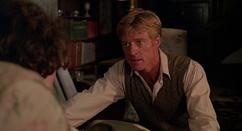 Movie still from “Out of Africa” (1985), directed by Sydney Pollack – A man sitting at a table in front of books; Close Up shot, Over the shoulder angle