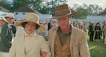 Movie still from “Out of Africa” (1985), directed by Sydney Pollack – A man and a woman walking in front of a group of people; Medium shot, Low angle