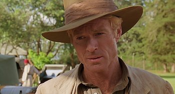 Movie still from “Out of Africa” (1985), directed by Sydney Pollack – A person wearing a hat with trees in the background; Close Up shot, Over the shoulder angle