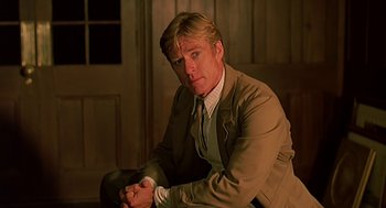 Movie still from “Out of Africa” (1985), directed by Sydney Pollack – A man in a suit and tie sitting in a room; Medium shot, Low angle