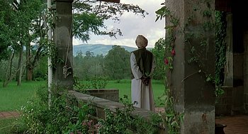 Movie still from “Out of Africa” (1985), directed by Sydney Pollack – A man in a long white coat standing on a porch; Wide shot, Over the shoulder angle