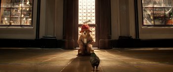 Movie still from “Paddington” (2014), directed by Paul King – A brown teddy bear sitting on the floor next to a bird; Wide shot, Low angle