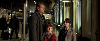 Movie still from “Paddington” (2014), directed by Paul King – A man standing next to two boys in a hallway; Medium shot, Over the shoulder angle