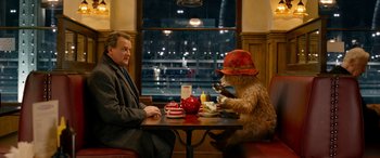 Movie still from “Paddington” (2014), directed by Paul King – A man sitting at a table next to a stuffed animal; Medium shot, Over the shoulder angle