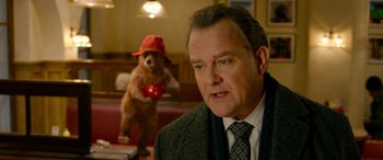 Movie still from “Paddington” (2014), directed by Paul King – A man in a suit and tie next to a teddy bear; Medium shot, Over the shoulder angle