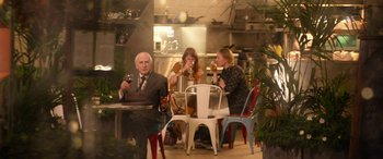 Movie still from “Paddington” (2014), directed by Paul King – A group of people sitting at a table drinking wine; Wide shot, Over the shoulder angle