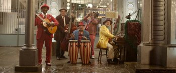 Movie still from “Paddington” (2014), directed by Paul King – A group of people playing musical instruments in a room; Wide shot, High angle