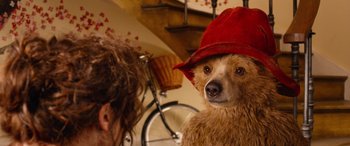 Movie still from “Paddington” (2014), directed by Paul King – A brown bear wearing a red hat with a bicycle in the background; Close Up shot, Over the shoulder angle