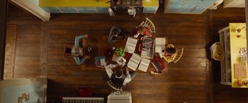 Movie still from “Paddington” (2014), directed by Paul King – A group of people sitting around a table with books; Wide shot, Overhead angle