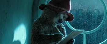 Movie still from “Paddington” (2014), directed by Paul King – A brown bear wearing a red hat writing on a piece of paper; Close Up shot, High angle