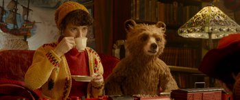 Movie still from “Paddington” (2014), directed by Paul King – A man sitting next to a teddy bear drinking a cup of coffee; Medium shot, Over the shoulder angle