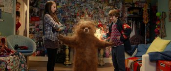 Movie still from “Paddington” (2014), directed by Paul King – Two people standing next to a brown teddy bear; Wide shot, Over the shoulder angle