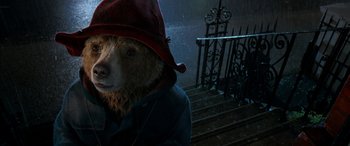 Movie still from “Paddington” (2014), directed by Paul King – A bear wearing a red hat standing next to a metal gate; Close Up shot, Low angle