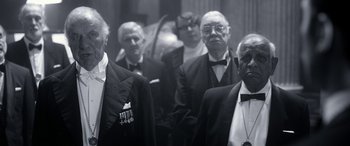 Movie still from “Paddington” (2014), directed by Paul King – A black and white photo of a group of men in tuxedos; Medium shot, Low angle