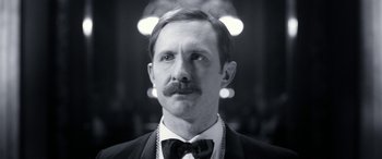 Movie still from “Paddington” (2014), directed by Paul King – A black and white photo of a man in a suit and bow tie; Close Up shot, Low angle