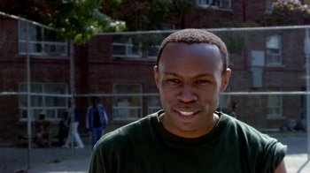 Movie still from “Paid in Full” (2002), directed by Charles Stone III – A young man smiles for the camera in front of a brick building; Close Up shot, High angle